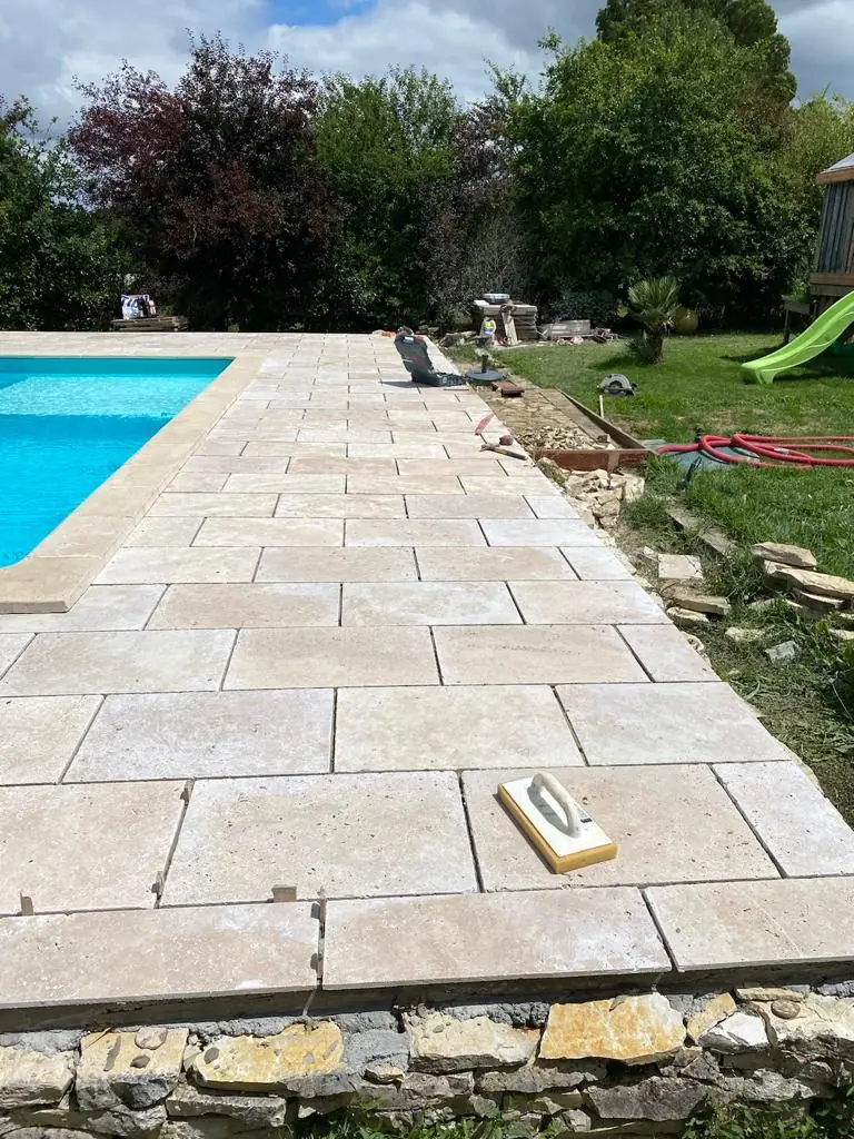 Dallage en pierre naturelle le long d'une piscine, finition aux joints en cours