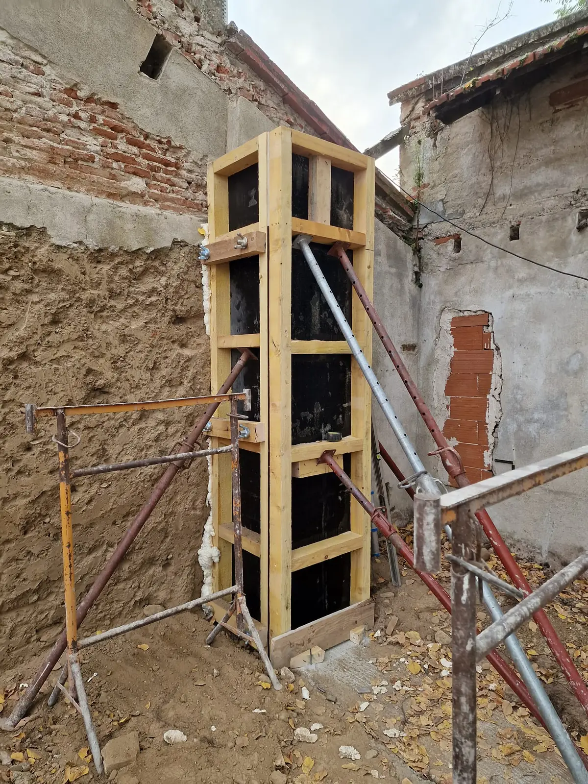 Coffrage bois d'un poteau béton contre un mur ancien lors d'une rénovation structurelle