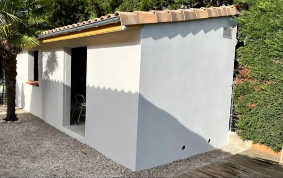 Bâtiment annexe rénové avec enduit neuf et toiture tuile, cour en gravier