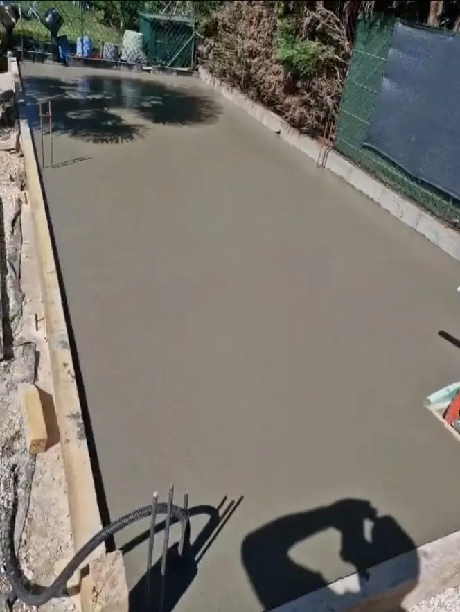 Terrasse béton fraîchement coulée dans un jardin clôturé
